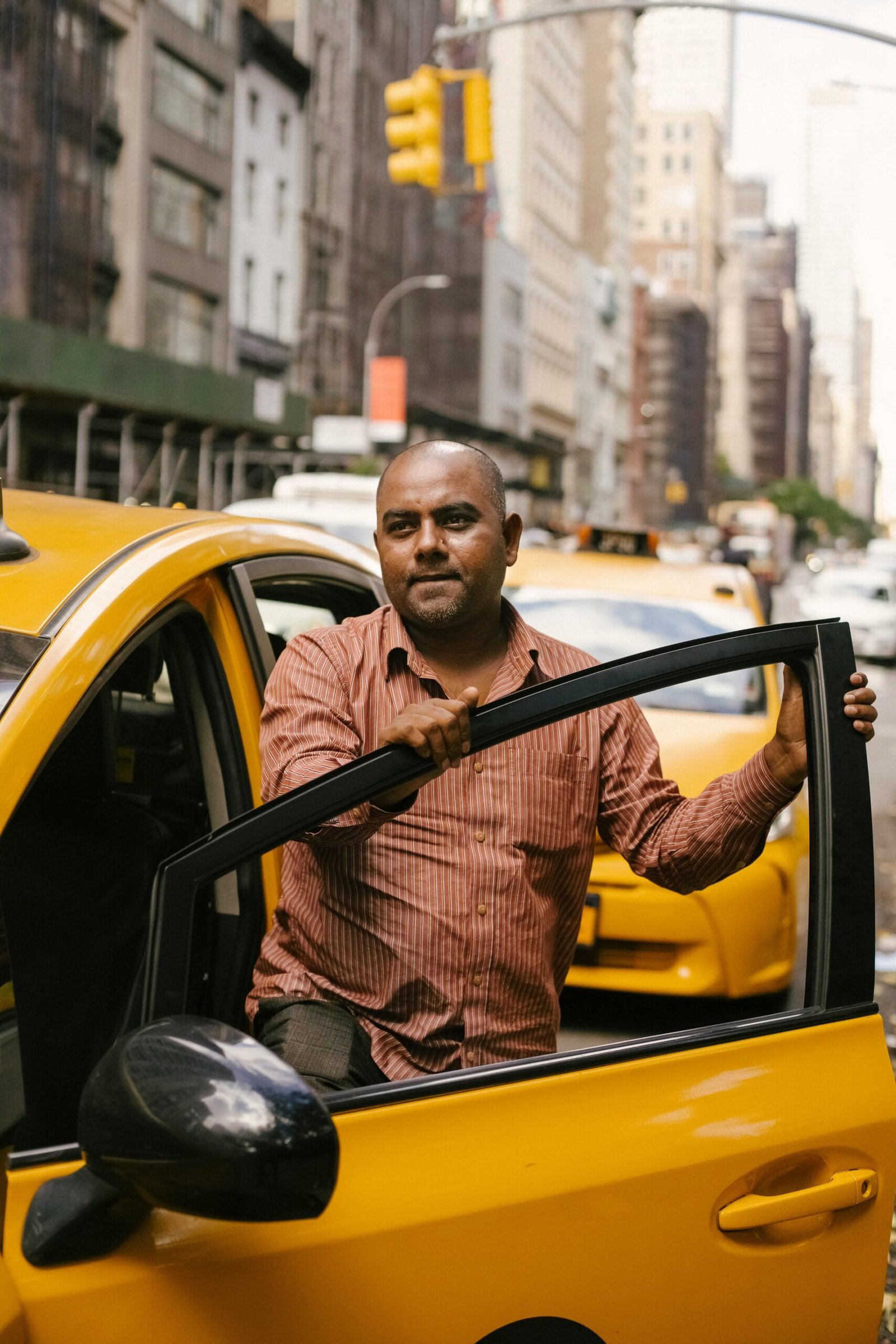 A taxi driver stepping out of a yellow cab in a busy city street during the day.